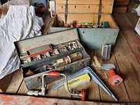 Image showing two metal tool boxes with assorted screws and hardware along with a wooden tool box, masonry trowel, hand drill, brace-like tool, and block tool on a wooden floor.