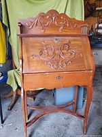 Front closed view of solid wood vintage secretary desk with carved scrollwork decoration and keyhole lock.