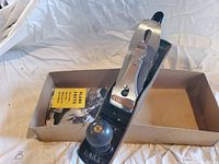 Stanley hand plane in box with front knob and blade adjustment lever visible, along with instruction manual.