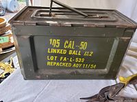 Front view of green military ammunition box with stencil text indicating it contains .50 caliber linked ball ammunition.