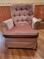 Front view of the pink velvet swivel rocker chair showing the tufted backrest, cushioned seat, and rolled armrests.