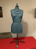 Front view of the vintage female dress form mannequin torso standing on a steel tripod base, covered in blue patterned fabric.