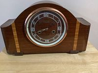 Full front view of the wooden mantle clock showing the curved top, wood grain, and clock face with keyhole.