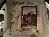 Front cover of Led Zeppelin IV LP showing a man carrying a large bundle of sticks against a rustic background with visible wear and peeling on the cover.