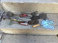 Overview of all nine vintage spatulas and egg flippers showing variety of handle styles and blade shapes; some painted wooden handles and perforated blades