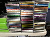 Photo shows multiple stacks of CD jewel cases arranged closely in three columns with various artist titles and collections visible.