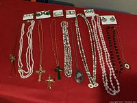 Full lot arranged on red surface showing all pieces including earrings on cards, multiple necklaces with cross pendants, beads, and pendants.