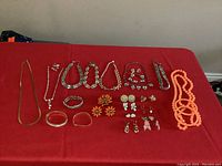 Full view of the 31 pieces of vintage costume jewelry on a red surface, including necklaces, earrings, bracelets, and sets.