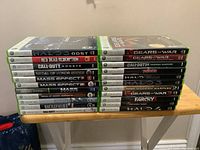 Stack of 22 Xbox 360 game cases on wooden table, titles visible on spines, showing mix of action and shooter games.