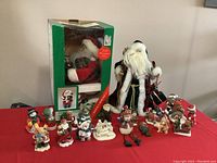 Overall display showing Father Noel standing next to musical Santa in box with 18 small assorted Christmas figurine ornaments arranged in front.