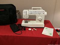 Singer Model 9818C sewing machine with free arm, power cord, foot pedal, bobbins, spool of thread and user manual on a red surface.