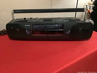 Front full view of Sony Radio Cassette-Corder CFS-W303 on red surface with carry handle extended.