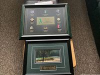 Two framed golf-related pieces on floor, one watercolour golf course painting and one history of golf championships pins collage.