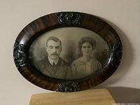 Full view of the vintage oval wooden frame with bubble glass and old black-and-white portrait of man and woman.
