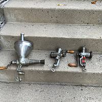 Three vintage metal manual meat grinders resting on concrete steps, showing various sizes and clamp mechanisms