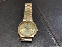 Top view of the gold-tone Whittnauer men's watch showing the round gold dial with date display and metal link bracelet.