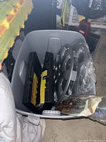 Photo of gray plastic bin containing roadside assistance flares, car rims, and other wrapped automotive items.