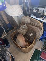 View of large collection of various wicker baskets and flat woven wicker panels or trays arranged inside a large rectangular basket in a garage