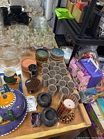 Photo showing various bowls, cups, coasters, black pottery jars and glassware arranged on shelves and table.