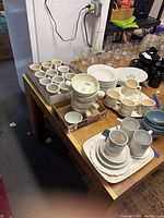 Overview of ceramic mugs, bowls, serving plates, saucers, and black cups on a table