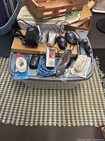 Photo of various computer mice, voice recorder, coax cables, and keyboard on a blue plastic storage bin on a checkered carpet