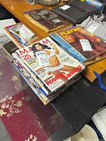 Top view of stacked magazines including Maxim featuring Roselyn Sanchez, Playboy magazine from 1983, and partially visible sports related magazines.