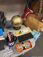 Overview photo showing all items in the lot: Pen set box, Tarzan watch container, blue dog mug, golden globe decor, and a white ceramic decorative item.