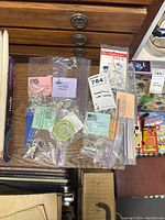 Photo showing multiple small sealed plastic bags containing metal miniature figures, replica dice, and wine bottle seal replicas with descriptive labels.