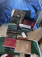 Multiple vintage books stacked and spread out on floor including large red, green, and brown bound books