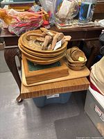 Wooden boards, bowls, elephant decor, and storage box shown stacked on and around a small wooden table.
