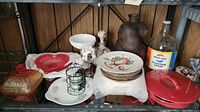 Shelf with assorted glass and decorative items including Murano glass, plates, brown jug, Pepsi-Cola bottle, and white pedestal bowl