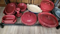 Overall wide view of the red ceramic bakeware collection on shelf including covered dishes, bowls, and baking trays