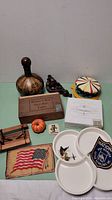 Photo showing the full assortment of small items on a green table including decorative bottle, cigar box, figurine, patches, food items, and dishes.