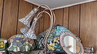 Photo showing three stained glass lampshades, metal floor lamp with three frosted glass lampshades, and stained glass framed mirror.