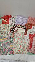Overhead photo showing 10 vintage aprons in assorted floral and patterned designs in various colors such as red, purple, pink, orange, and green, some with lace or ruffle trim.