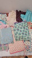 Photo showing various folded aprons with distinct floral and patterned designs including light blue, teal, and cream colors.