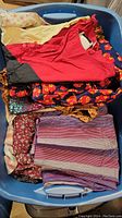 Assorted vintage clothing items in a blue tote showing multiple colors, fabrics, and patterns including solids and florals.