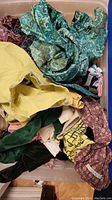 Top-down view of vintage clothing items including paisley and solid color fabrics in a plastic tote