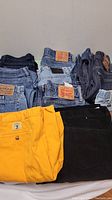 Overview showing multiple pairs of blue denim jeans and colored pants laid in two rows