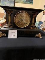 Antique black mantle clock with gold-tone decorative columns, feet, and an ornate clock face with Arabic numerals.