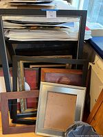 Image showing a collection of various picture frames in multiple sizes and finishes leaning against a wall and furniture.