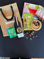 Front view of all lot items arranged on a black surface, showing the tote, beer coozie, wine charms, wine opener, books, and cans