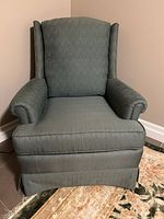 Front view of the green fabric wingback armchair showing padded arms, high backrest, and cushioned seat.