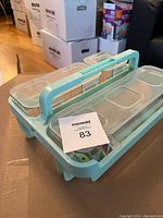 Light blue plastic craft caddy with six clear compartments and a handle, sitting on a cardboard box.