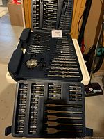 Two open black plastic cases showing a large assortment of metal drill and screwdriver bits in organized slots.