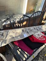 Photo showing rolled upholstery fabric with leaf pattern in neutral tones, and piled folded pink, red, and black fabric pieces underneath on a chair.