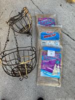 Photo of a two tiered hanging metal basket with decorative scroll design and three packs of burlap wrap for protecting shrubs or plants.