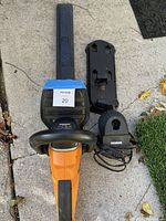 WORX hedge trimmer lying on ground with blade cover, battery pack, and charger unit.