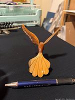 Wooden hummingbird figurine showing outstretched wings and fan-shaped tail with pen for size reference.