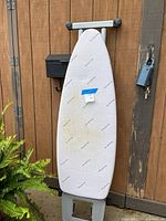 Ironing board folded and standing upright against a wooden door, showing the padded fabric surface with minor discolorations.